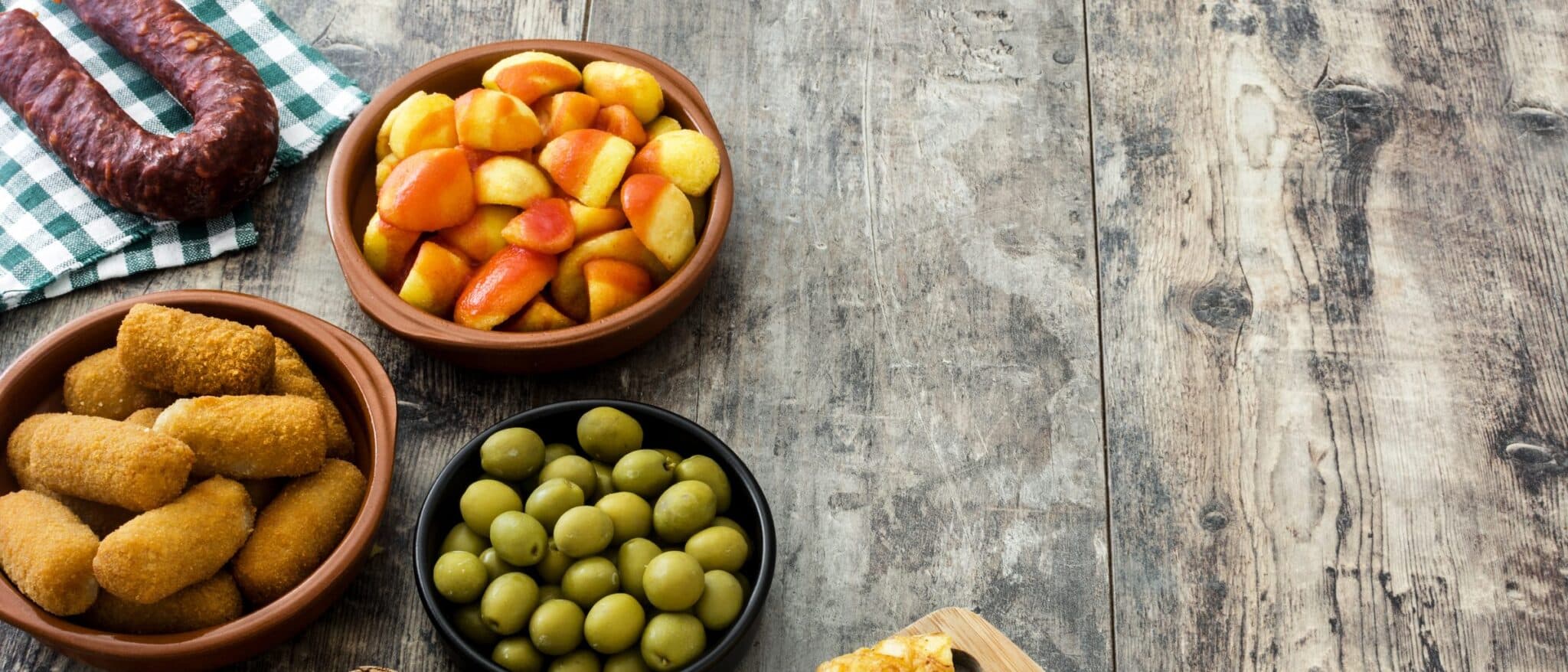 Croquetas, patatas bravas, olives and chorizo on a rustic wooden table
