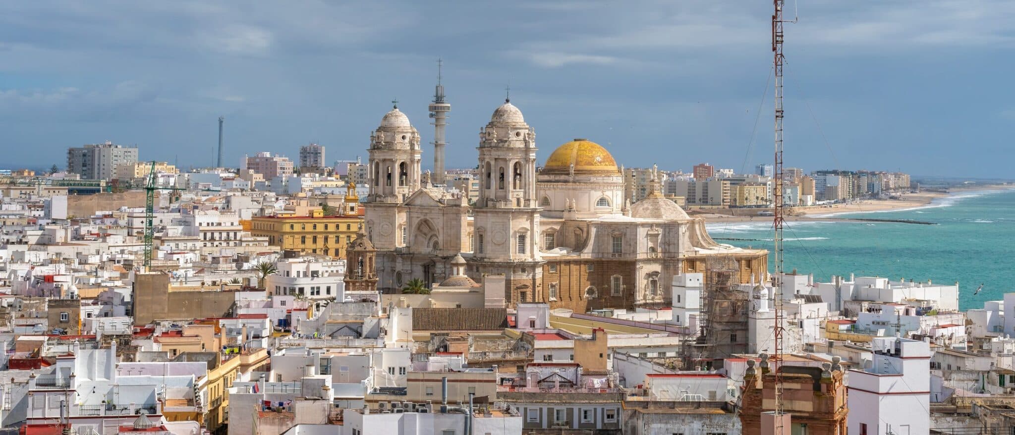 Cádiz old town from above, the cathedral's golden dome among white rooftops, with the Atlantic beach beyond