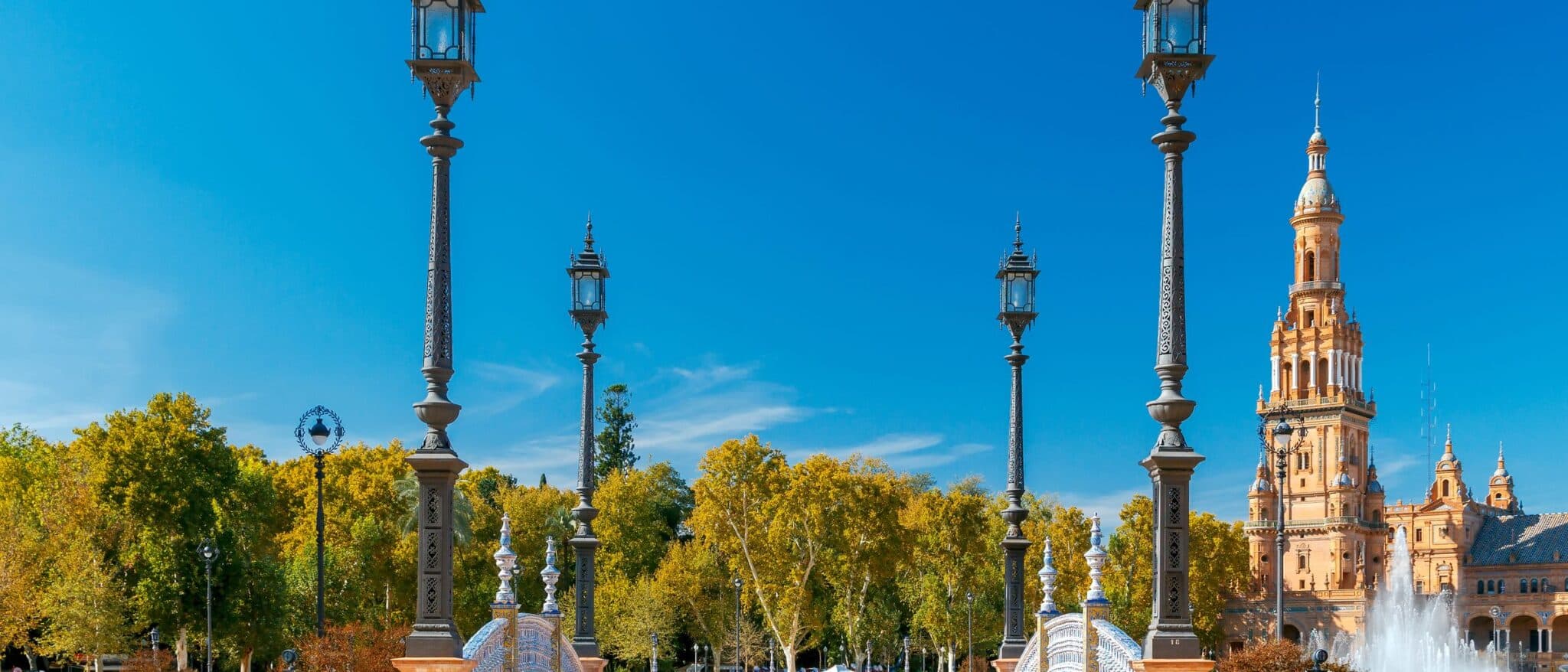 Plaza de España in Seville: a tiled bridge, iron lamps and the north tower, with the plane trees turning yellow