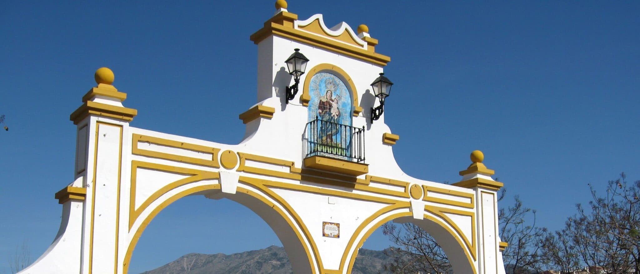The white and yellow entrance arch of Fuengirola's Recinto Ferial, with a tiled image of the Virgen del Rosario above the central arch